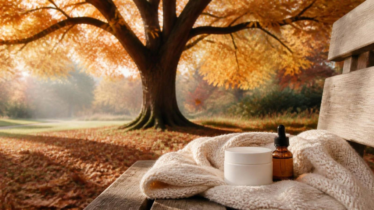 A golden autumn tree in morning light with a jar of moisturiser and a dropper bottle on a knitted scarf
